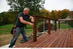 a man is standing on a wooden deck with his hand on the rail and looking at something in front of him