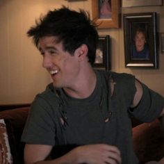 a young man sitting on top of a couch next to a wall covered in pictures