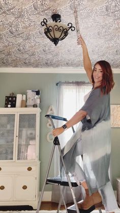 a woman standing on top of a ladder in a room with a chandelier