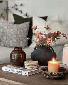 a coffee table with candles, books and flowers on it in front of a couch