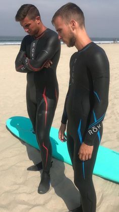 two men in wetsuits standing on the beach