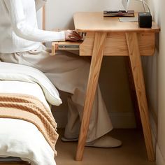 a woman sitting at a small table with a lamp on it next to a bed