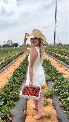 a woman in a straw hat holding a box of strawberries on a farm field