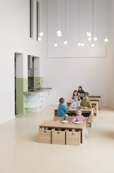 children are sitting at desks in the middle of a room with lights hanging from the ceiling