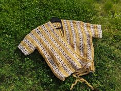 a yellow and white crocheted sweater laying on the ground next to some grass