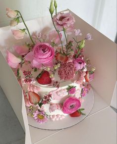 a white cake with pink flowers and strawberries on top is in a cardboard box