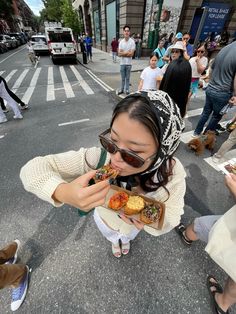 a woman eating food while standing on the side of a road in front of people