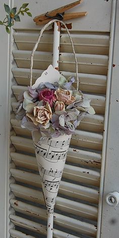 a white vase with flowers and music notes hanging from it's side on a window sill