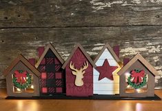 three wooden houses decorated with christmas decorations and lights on top of a wood table next to a wall