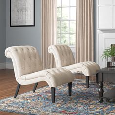 two white chairs sitting on top of a rug in front of a table and fireplace