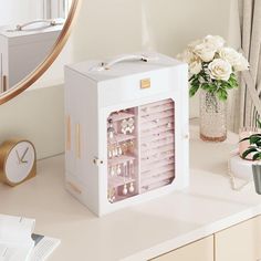 a white jewelry box sitting on top of a table next to a mirror and flowers