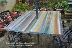 an outdoor dining table made out of wood and wrought iron legs with colorful paint on it