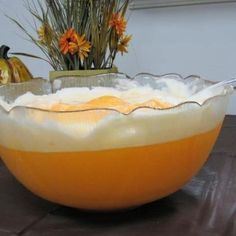 an orange and white bowl sitting on top of a wooden table next to some flowers