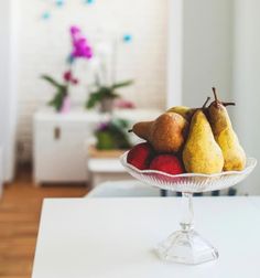 a glass bowl filled with fruit on top of a white kitchen counter next to a window