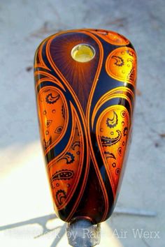 an orange and blue glass vase sitting on top of a metal pole with a light shining through it