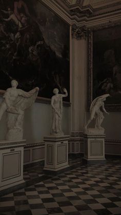 three statues in a room with paintings on the wall