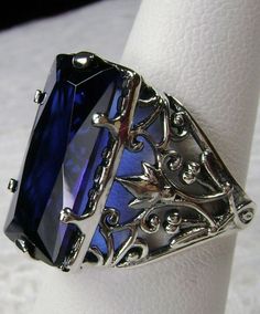 Simulated Blue Sapphire Ring Baguette Design#32 Custom Inspired by the intricate Victorian designs of the late 1800s, I now offer this gorgeous filigree Antique reproduction in sterling silver. The lovely ring is set with a flawless 7ct Blue sapphire gemstone. The baguette rectangle-cut simulated blue sapphire is 18mm long by 9mm wide. The ring is 8mm of the finger. The inside of the band is marked 925 for sterling. Notice the intricate and floral design of the silver filigree setting and band. Formal Sapphire Ring With Rectangular Stone, Sapphire Ring With Rectangular Stone For Formal Occasions, Blue Rectangular Diamond Cut Jewelry, Elegant Blue Emerald-cut Jewelry, Formal Sapphire Rings With Rectangular Stone, Formal Sapphire Jewelry With Rectangular Stone, Formal Blue Emerald Cut Jewelry, Elegant Blue Sapphire Ring For Formal Occasions, Formal Rectangular Sapphire Ring In Sterling Silver