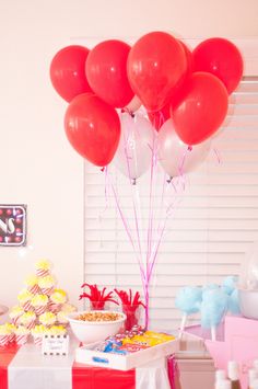 red and white balloons are in the air above a table filled with candy, cake and other items