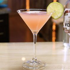 a pink drink with a lime slice on the rim in front of two vodka bottles