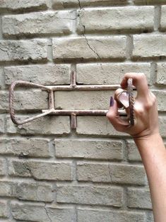 a person is holding up an old metal tool on a brick wall with nails in it