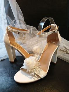 Complete your stunning bridal ensemble with these off-white bridal sandals featuring delicate organza flower clips. These elegant shoes boast a timeless block heel and flattering open toe design, ensuring both style and comfort on your special day. Perfect for the bride or bridesmaid, these high heels showcase a beautiful floral design that will elevate any wedding outfit. Make a statement as you walk down the aisle in these exquisite pumps, adding a touch of romance to your wedding look. Colour White Flower-shaped Elegant Sandals, Elegant Floral Embellished Sandals For Weddings, White Formal Wedding Shoes With Flower Design, Elegant Floral Embellished Wedding Sandals, White Bridal Accessories With Ankle Strap For Evening, White Bridal Accessories With Ankle Strap For Wedding, Elegant Flower Heels For Wedding, White Flower Wedding Shoes, White High Heel Shoe Clips For Wedding