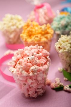 several small plastic cups filled with popcorn on a pink tablecloth, some have sprinkles in them