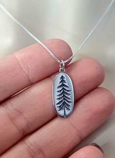 This minimalist Pine Tree Necklace makes the perfect Anniversary, Birthday or Christmas Gift!  Featuring a Solid .925 Sterling Silver 1 inch Pine Tree Oval Pendant and a Solid .925 Sterling Silver Cable or Box Chain. Perfect for everyday wear. Choice of Necklace Gift Box. Add a Birthstone to this Necklace here: https://www.etsy.com/listing/886396220/sterling-silver-tiny-swarovski-crystal?ref=shop_home_active_3&crt=1 Click on Link to Shop our Etsy Store: https://www.etsy.com/shop/LastingMemoryJewelry Pine Cone Jewelry, Pine Jewelry, Tree Jewelry, Wanderlust Jewelry, Forest Pendant, Hiking Jewelry, Nature Jewelry, Mountain Necklace, Mountain Jewelry, Best Seller, Autumn Jewelry, Fall Jewelry, Christmas Jewelry, Christmas Gift, Anniversary Gift, Birthday Gift, Gift for Her, Gifts for girlfrie Pine Tree Jewelry, Hiking Jewelry, Pine Cone Jewelry, Pine Jewelry, Tiny Cross Necklace, Silver Initial Charms, Initial Necklace Silver, Wanderlust Jewelry, Woodland Jewelry