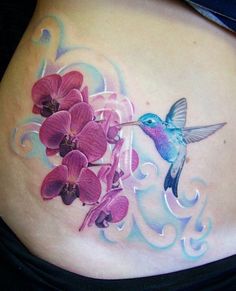 a woman's stomach with pink flowers and a hummingbird on the side tattoo