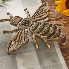 a metal bee sitting on top of a table next to a sunflower and vase