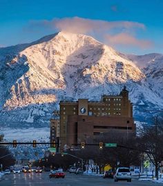 the mountains are covered in snow as cars drive down the road near buildings and traffic lights