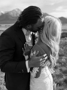 a man in a suit kissing a woman on the forehead with mountains in the background