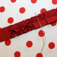 a red piece of fabric with some thread on it and white polka dot tablecloth