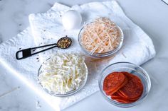 three bowls with different types of food in them on a white towel next to an egg, pepperoni and cheese