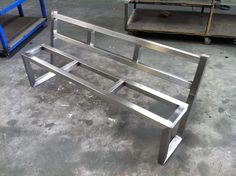 a metal bench sitting on top of a cement floor next to a blue dolly and some shelves