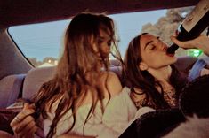 two women sitting in the back seat of a car and one is drinking from a bottle