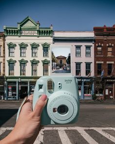 a person holding up a camera in front of some buildings on a street with no cars