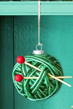 yarn ball ornament hanging on green door with knitting needles and balls of yarn