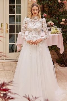 a woman standing in front of a table wearing a white wedding dress with long sleeves