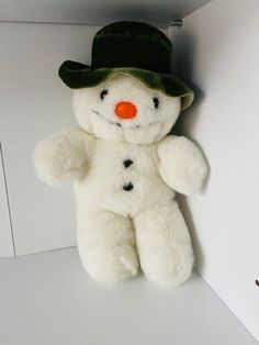 a white teddy bear with a green hat on it's head and nose sitting in a corner