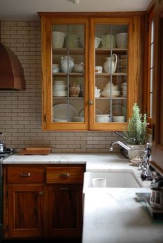 a kitchen with wooden cabinets and white dishes on the counter top, next to an oven