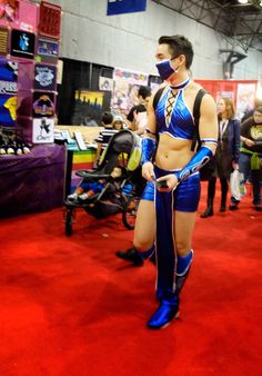 a woman in blue and black cosplay standing on a red carpet with other people