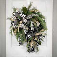 a wreath is hanging on the front door with black and white ribbons, pine cones, and feathers