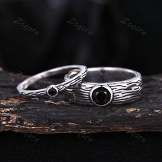 two silver rings with black stones are sitting on top of a piece of drift wood