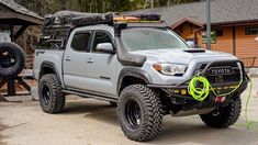 a gray truck parked in front of a wooden building with a green hose attached to it