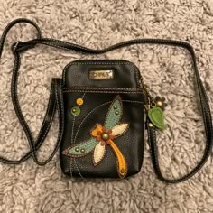 a small black purse with a dragonfly on it's front and shoulder strap