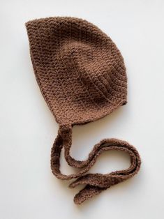 a crocheted brown hat with a string attached to the brim is laying on a white surface