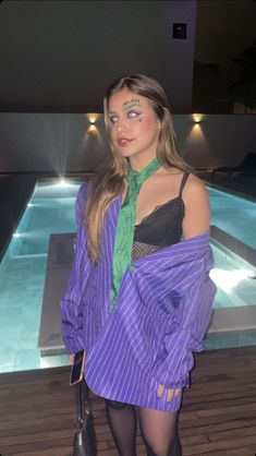 a woman with makeup on her face standing next to a pool wearing a purple shirt and green tie