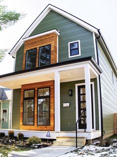 a green house with white trim and wood accents on the front door is shown in winter