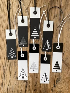 six tags with black and white designs hanging from strings on a wooden table, one has a string attached to it