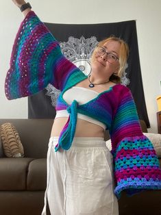 a woman is wearing a colorful knitted sweater and holding her arms in the air